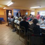 grupa Seniorów siedzi za stołem na spotkaniu w MOPS